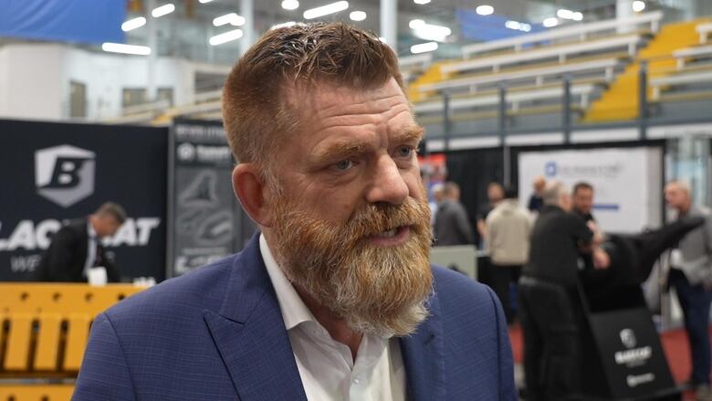 A young man with a large, red, gray beard, wearing a suit.